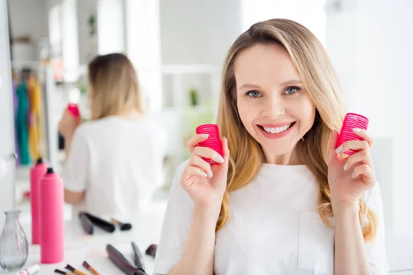 Retrato de atractiva chica rubia alegre glamorosa sosteniendo rodillos haciendo la preparación del cabello en el hogar blanco claro en el interior —  Fotos de Stock