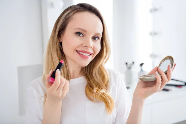 Retrato de chica alegre atractiva mirando el espejo aplicando bálsamo en los labios preparando en casa blanca luz interior —  Fotos de Stock