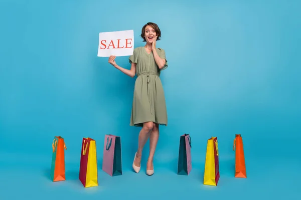 Volledige lengte foto van verbaasd vrolijke jonge vrouw hand banner verkoop face bags nieuws geïsoleerd op blauwe kleur achtergrond — Stockfoto