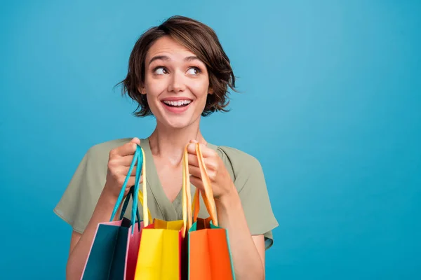 Foto van zoete jonge brunette dame hold tassen kijken leeg ruimte slijtage kaki jurk geïsoleerd op blauwe kleur achtergrond — Stockfoto