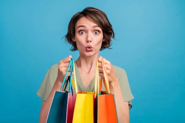 Foto de la joven morena impresionada sostiene bolsos usan vestido caqui aislado sobre fondo de color azul — Foto de Stock