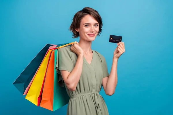 Foto de otimista millennial morena senhora segurar sacos cartão desgaste vestido cáqui isolado no fundo de cor azul — Fotografia de Stock