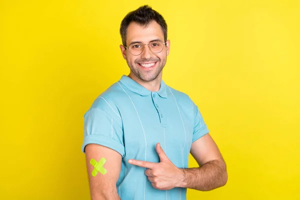Bild av optimistisk brunett man punkt hand gips slitage glasögon blå t-shirt isolerad på gul färg bakgrund — Stockfoto