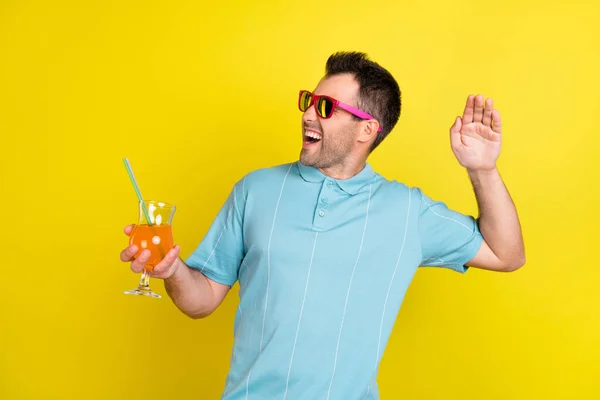Foto do homem morena engraçado segurar cocktail olhar espaço vazio desgaste óculos azul t-shirt isolado no fundo de cor amarela — Fotografia de Stock