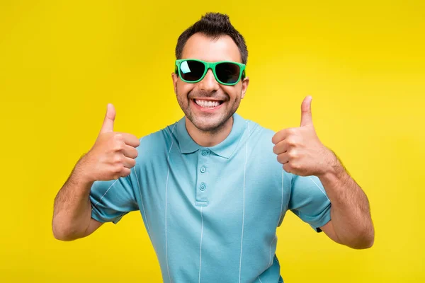 Zdjęcie fajny brunet człowiek pokazać kciuk do góry nosić okulary niebieski t-shirt izolowane na żółtym tle kolor — Zdjęcie stockowe