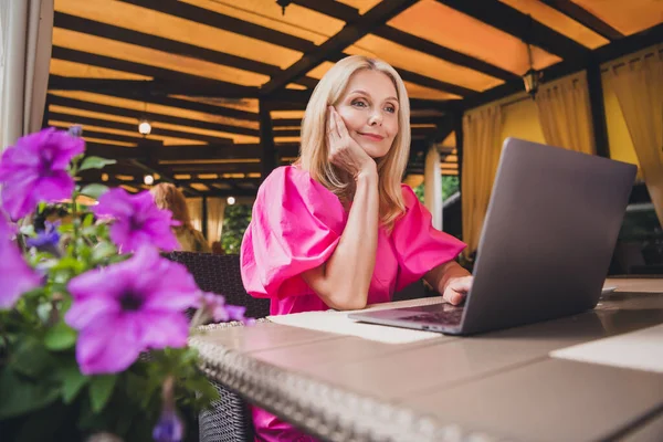 Foto portrét starší žena krásná atraktivní s blond vlasy sedí v kavárně na sobě růžové šaty procházející internet s notebookem — Stock fotografie