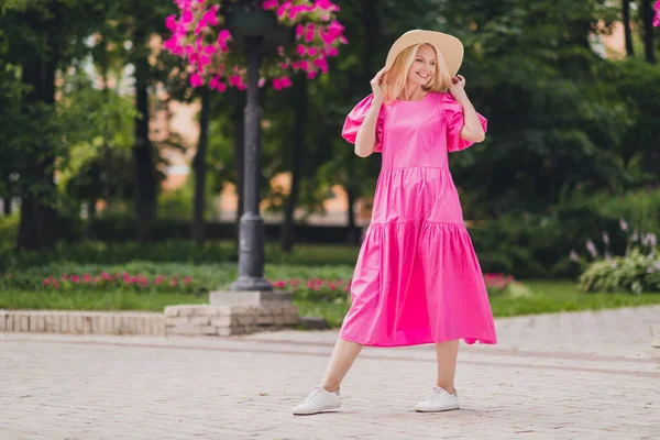 Zdjęcie marzycielskiej uroczej emerytki noszącej różowy strój ręce ramiona nakrycia głowy uśmiechające się spacerując poza ulicą miejską — Zdjęcie stockowe