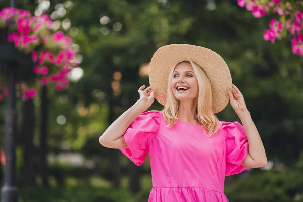 Фото сладко взволнованной женщины на пенсии носить розовый наряд руки руки головной убор улыбается прогулка за городской улице — стоковое фото