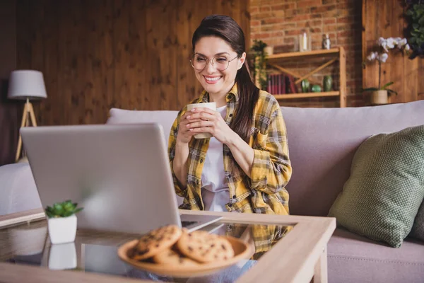 Foto van jonge vrolijke vrolijke vrouw dragen bril houden kopje thee kijken video laptop binnen huis — Stockfoto