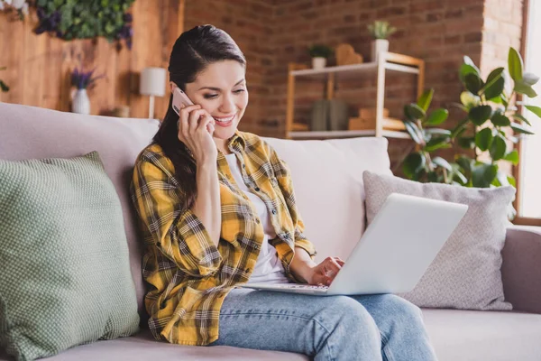 Foto de persona encantadora positiva sentada en el sofá uso netbook hablar teléfono tienen buen humor fin de semana en el interior —  Fotos de Stock