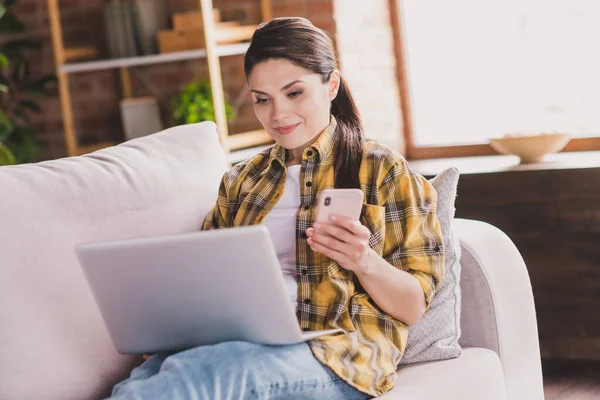 Foto di persona piuttosto positiva sedersi sul divano tenere telefono uso netbook social network hanno buon umore casa al chiuso — Foto Stock