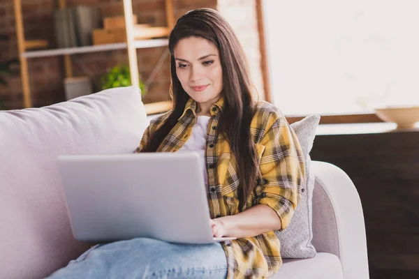 Zdjęcie pozytywne lady siedzieć wygodne kanapa trzymać laptop wpisując surf social network nosić koszulę kratę domu w pomieszczeniach — Zdjęcie stockowe