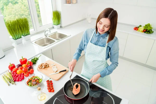 Над високим кутом зору портрет привабливої веселої досвідченої дівчини, яка готує корисну страву лососевий стейк вдома легка біла кухня — стокове фото