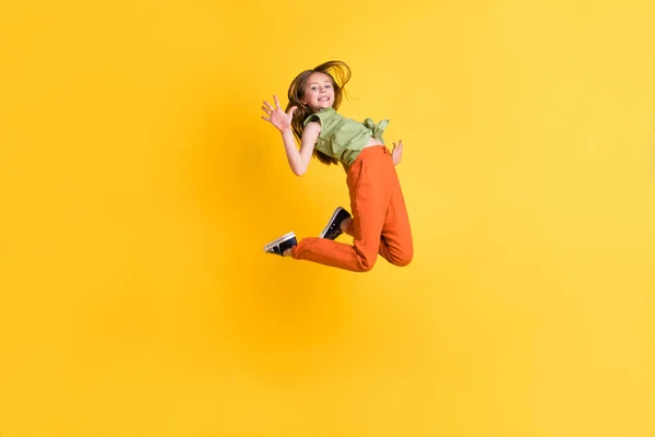 Фотография маленькой девочки в полный рост, подпрыгивающей без рук, изолированной ярким желтым цветом на фоне — стоковое фото