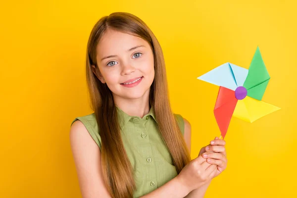 Foto portret schoolmeisje dragen groene shirt glimlachen spelen met windmolen geïsoleerde levendige gele kleur achtergrond — Stockfoto