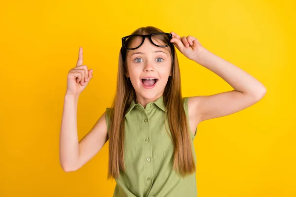 Photo de hourra blond petite fille tenir les lunettes point vers le haut porter blouse kaki isolé sur fond de couleur jaune — Photo