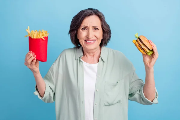 Fényképezés portré idős nő ing eszik egészségtelen junk food elszigetelt pasztell kék szín háttér — Stock Fotó