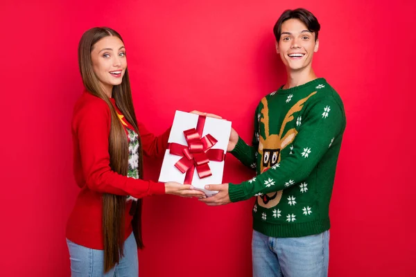 Foto de pareja positiva sostenga paquete decorado presente desgaste suéter feo aislado color rojo fondo — Foto de Stock