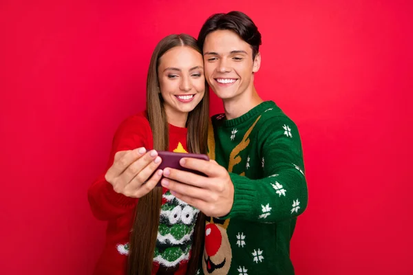 Foto de alegre pareja agradable chico mantenga el teléfono hacer selfie desgaste suéter feo aislado fondo de color rojo —  Fotos de Stock