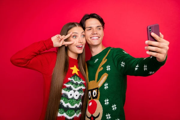 Foto van blij stel meisje show v-teken jongen nemen telefoon selfie dragen lelijk pullover geïsoleerde rode kleur achtergrond — Stockfoto