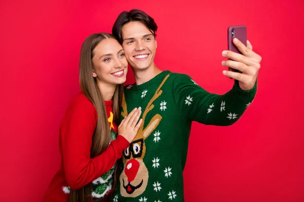 Foto de alegre pareja lindo chico mantenga el teléfono disparar selfie desgaste feo adorno suéter aislado de color rojo fondo —  Fotos de Stock