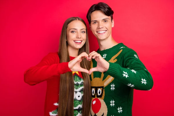 Foto di allegro due amanti dita dimostrano figura del cuore indossare maglione brutto isolato colore rosso sfondo — Foto Stock