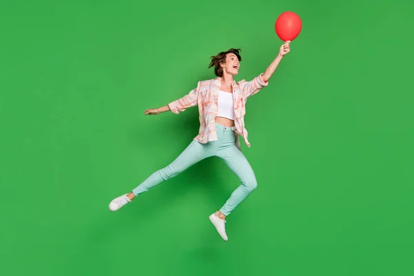 Повна довжина фото позитивної щасливої молодої жінки підстрибує вгору, посмішка червоної кулі ізольована на фоні зеленого кольору — стокове фото