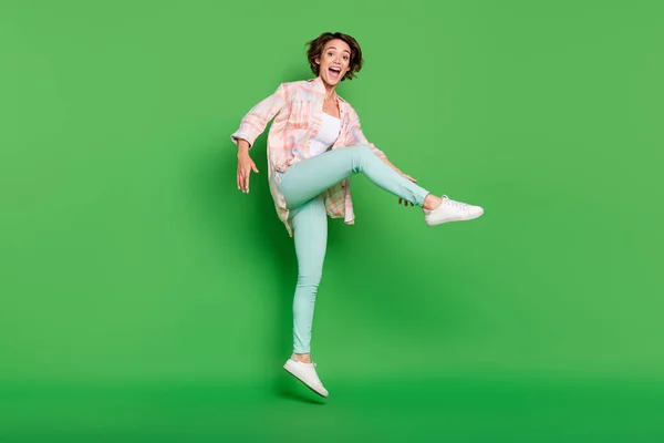 Plné tělo fotografie veselé pozitivní vzrušená žena skok nahoru držet nohu těšit izolované na zeleném pozadí — Stock fotografie