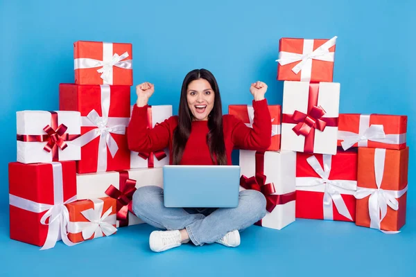 Portrait de belle fille gaie assise parmi les cadeaux à l'aide d'un ordinateur portable se réjouissant d'avoir du plaisir isolé sur fond de couleur bleu vif — Photo