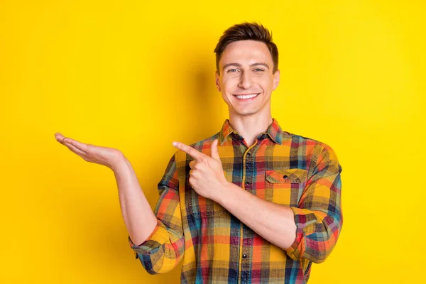 Портрет привабливого веселого хлопця, який тримає на долоні, демонструючи копію порожнього простору ізольованого на яскраво-жовтому кольоровому фоні — стокове фото