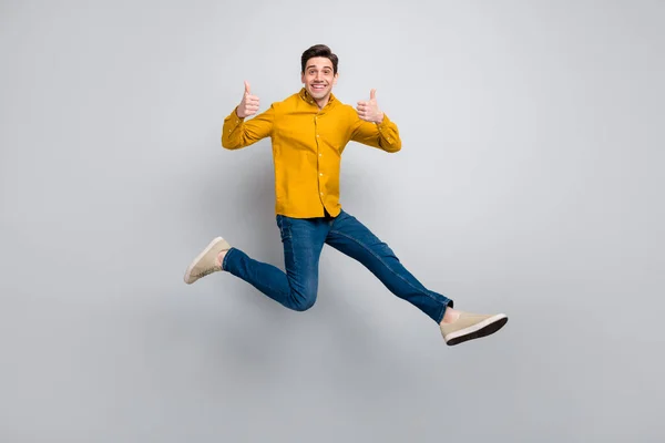 Tamanho do corpo de comprimento total vista de homem alegre atraente pulando mostrando polegar isolado sobre fundo de cor cinza — Fotografia de Stock