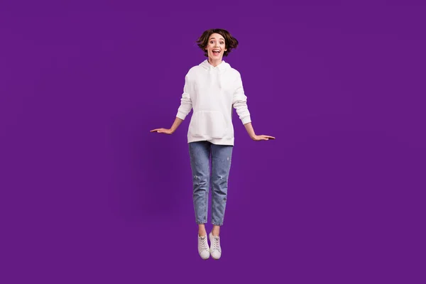 Foto in voller Größe von jungen attraktiven schönen Mädchen springen tragen weißen Pullover und Jeans isoliert auf violettem Hintergrund — Stockfoto