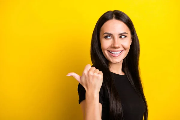 Foto de señora positiva pulgar directo espacio vacío mirar lado brillante sonrisa desgaste negro camiseta aislado color amarillo fondo — Foto de Stock