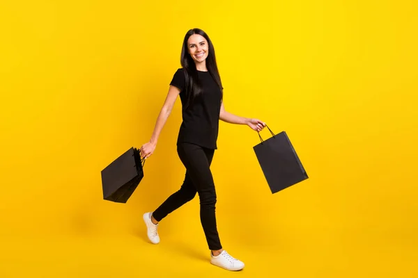 Full size profiel foto van charmante meisje lopen handen houden tassen kijken camera geïsoleerd op gele kleur achtergrond — Stockfoto