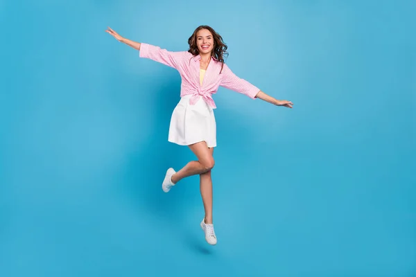 Фото блестящей красивой молодой женщины, одетой в белую юбку, улыбающейся, весело прыгающей на высоком голубом фоне — стоковое фото