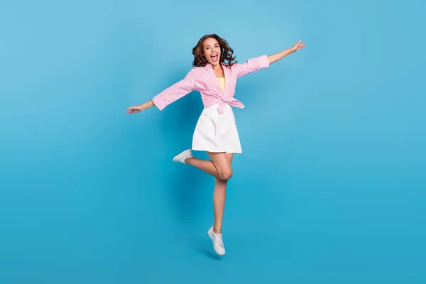 Фото милой очаровательной юной леди носить розовую рубашку прыгая высокие стороны рук улыбаясь изолированный синий цвет фона — стоковое фото