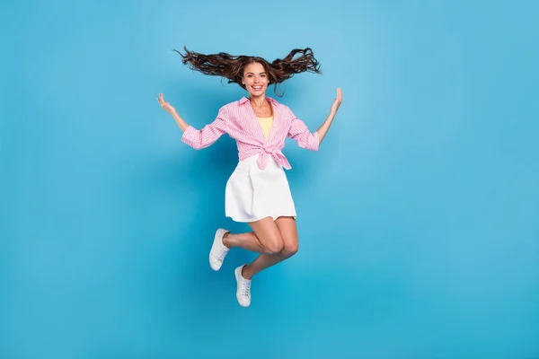 Foto de brilhante encantador jovem mulher vestida saia branca sorrindo mãos subindo braços saltando alto isolado fundo cor azul — Fotografia de Stock