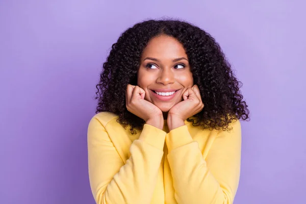 Foto de sonho bonito pele escura mulher usar camisola amarela sorriso braço bochechas olhando espaço vazio isolado cor violeta fundo — Fotografia de Stock