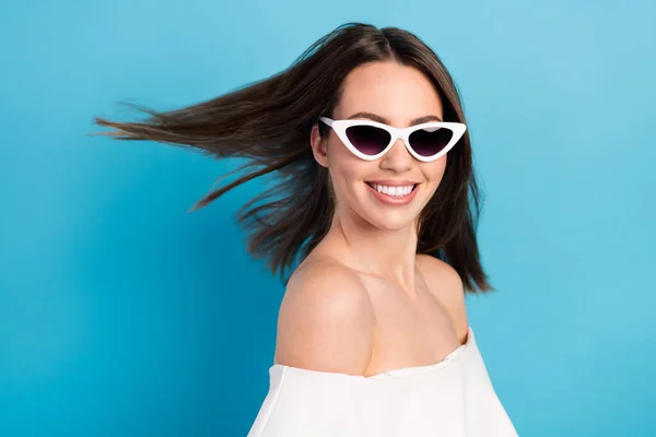 Foto de bonito brilhante jovem mulher vestida blusa branca óculos escuros vento soprando sorrindo isolado azul cor de fundo — Fotografia de Stock