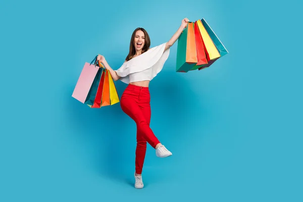 Photo of shiny exited young lady wear off-shoulders shirt walking holding shopping bags smiling isolated blue color background