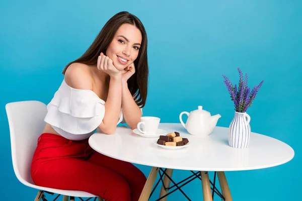Portret van aantrekkelijk vrolijk mooi meisje zitten aan tafel het eten van suikerzoet snoep lunch geïsoleerd over helder blauwe kleur achtergrond — Stockfoto