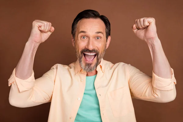 Photo de l'homme étonné joyeux lever les poings célébrer victoire porter chemise beige isolé fond de couleur brune — Photo