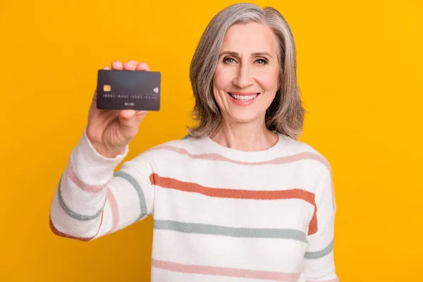 Foto de brilhante bonita senhora pensioner desgaste listrado pulôver segurando cartão de crédito sorrindo isolado cor amarela fundo — Fotografia de Stock