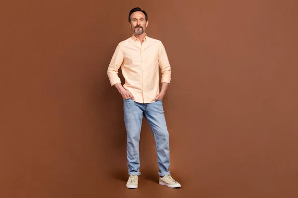 Foto van zelfverzekerde succesvolle zakenman handen zakken dragen beige shirt jeans geïsoleerde bruine kleur achtergrond — Stockfoto