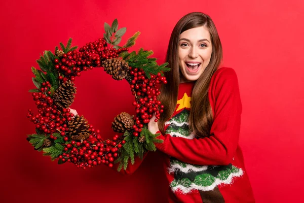 Фото позитивної молодої веселої жінки тримає руку вінок посмішки традиції Різдва ізольовані на червоному тлі — стокове фото