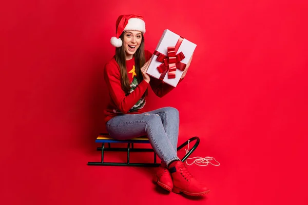 Full längd foto av glada glad positiv kvinna sitta pulka hålla presentförpackning isolerad på röd färg bakgrund — Stockfoto