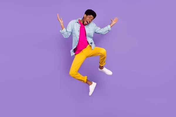 Foto di sciocco indiziato afro ragazzo salto alzare le mani indossare pantaloni camicia blu calzature isolato colore viola sfondo — Foto Stock
