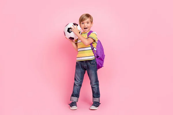 Lunghezza completa foto di giovane piccolo ragazzo indossare zaino tenere per mano il calcio buon umore isolato su sfondo di colore rosa — Foto Stock