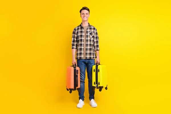 Foto de chico positivo alegre llevar dos maleta sonrisa dentada llevar camisa a cuadros aislado color amarillo fondo —  Fotos de Stock