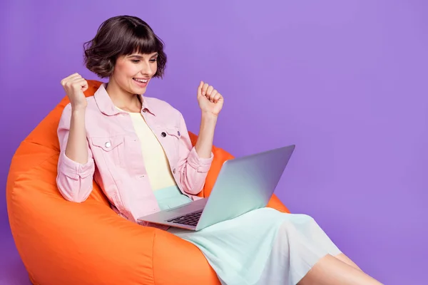 Foto av glad glad glad ung kvinna vinnare hålla handen dator gott humör sitta stol isolerad på violett färg bakgrund — Stockfoto